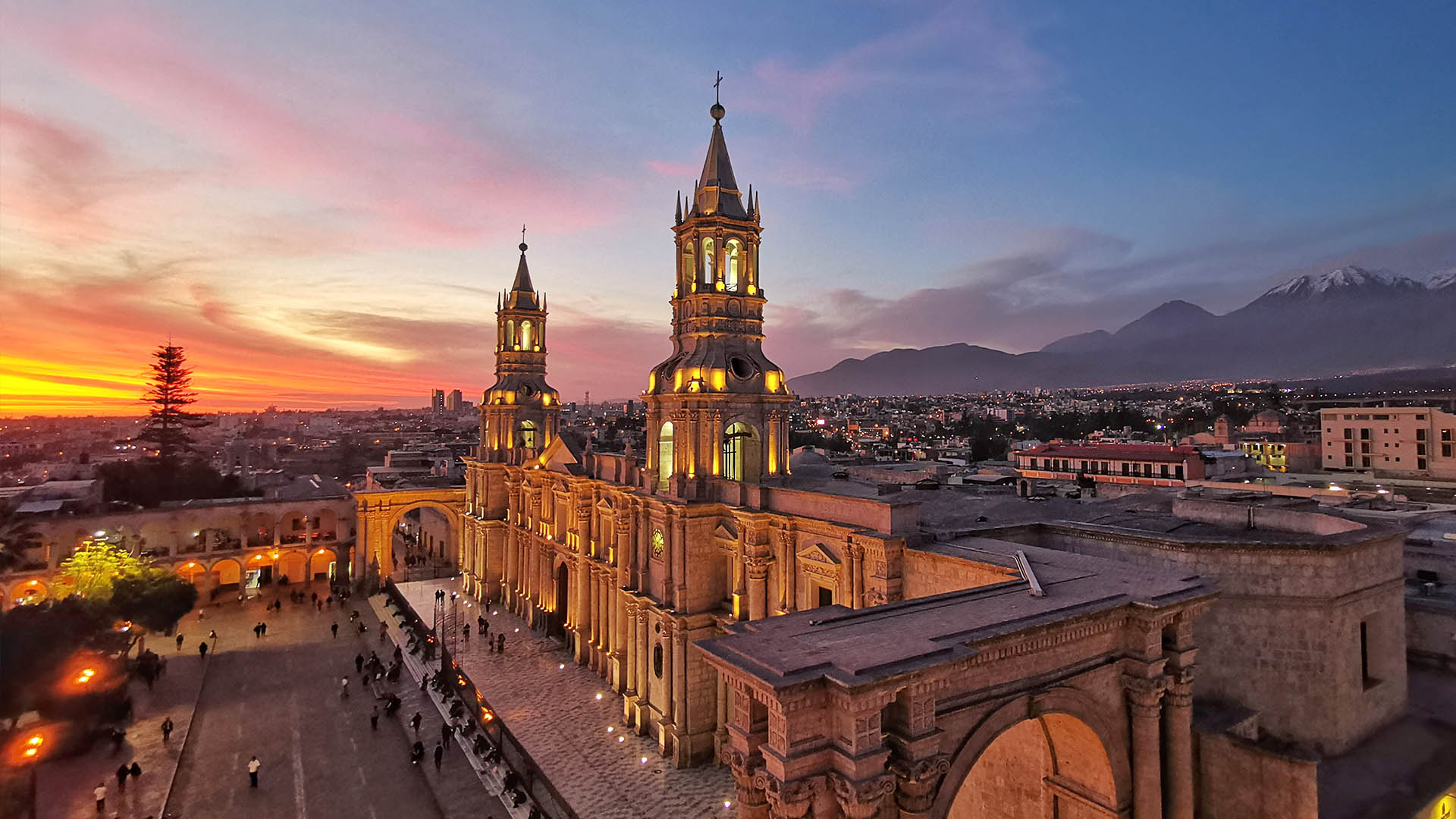 Illuminated facade of the Arequipa Cathedral and colonial arches made of white volcanic sillar stone at night.